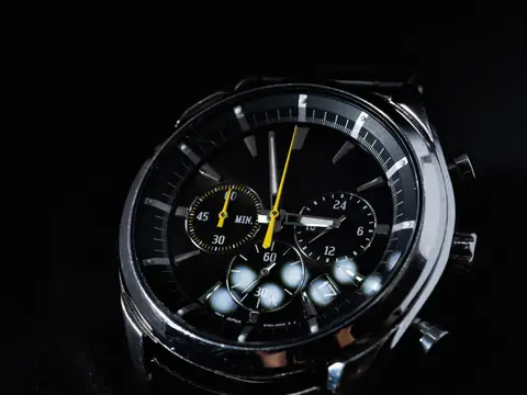 A steel chronograph wristwatch with a black dial, subdials and a yellow second hand on a black background