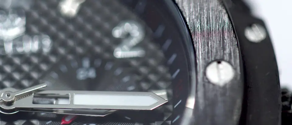 A close view of a wristwatch with a textured dark dial and a bezel held by exposed screws