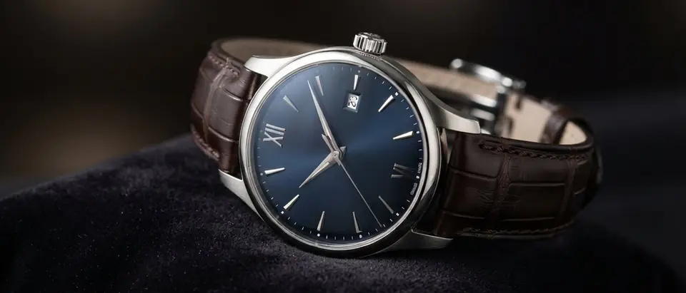 An elegant dress wristwatch with a deep blue dial, Roman numerals and a brown leather strap resting on dark velvet