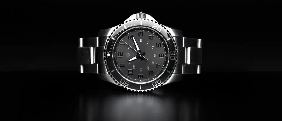 A steel sports wristwatch with a black dive bezel and a metal bracelet on a black background